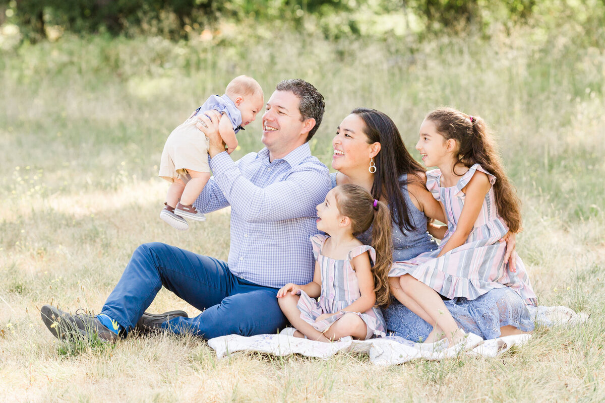 family of five seated in a meadow at champoeg state park for family photos
