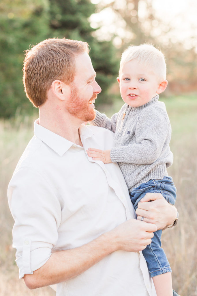 father and toddler son standing together in a field 