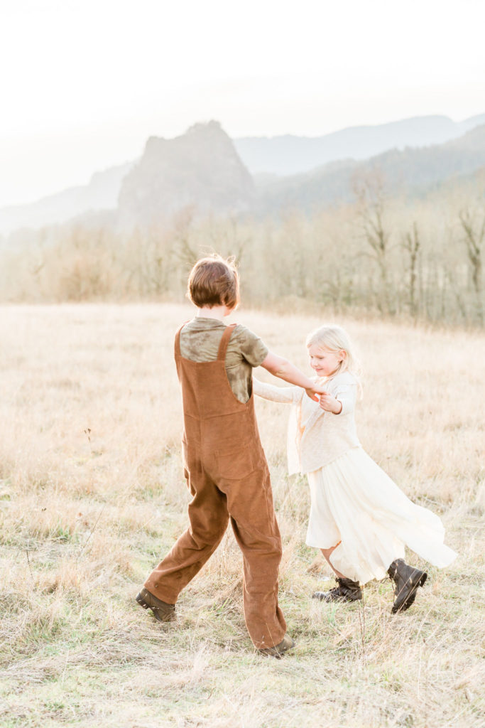two girls at a sisters photoshoot dancing in a field with a mountain in the background: photo ideas for siblings
