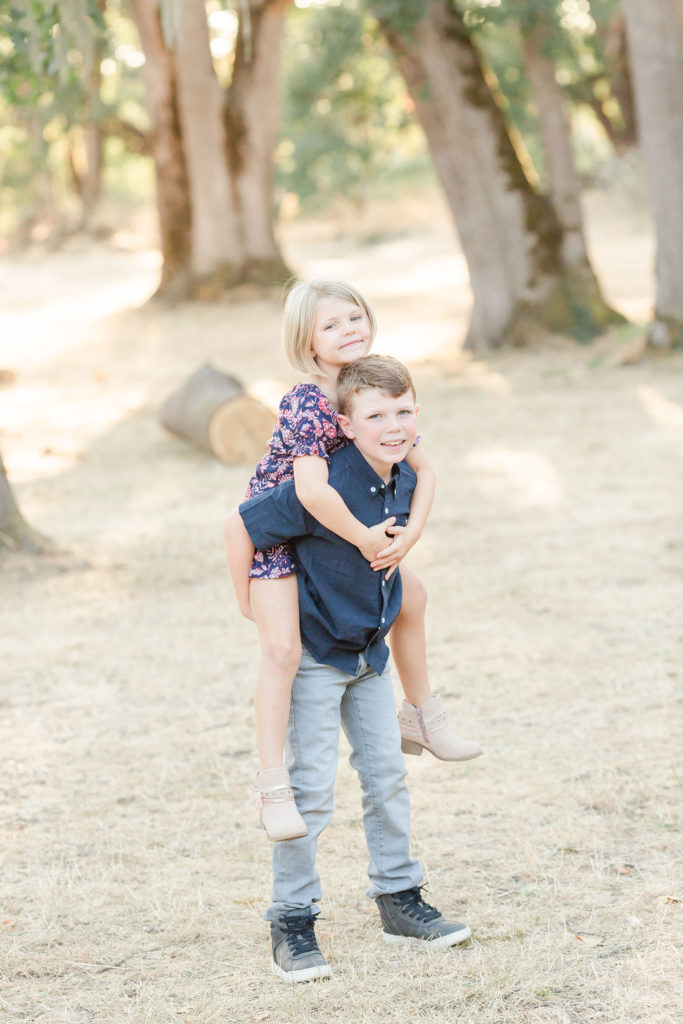 Big brother gives little sister a piggyback ride during sibling pictures: photo ideas for siblings