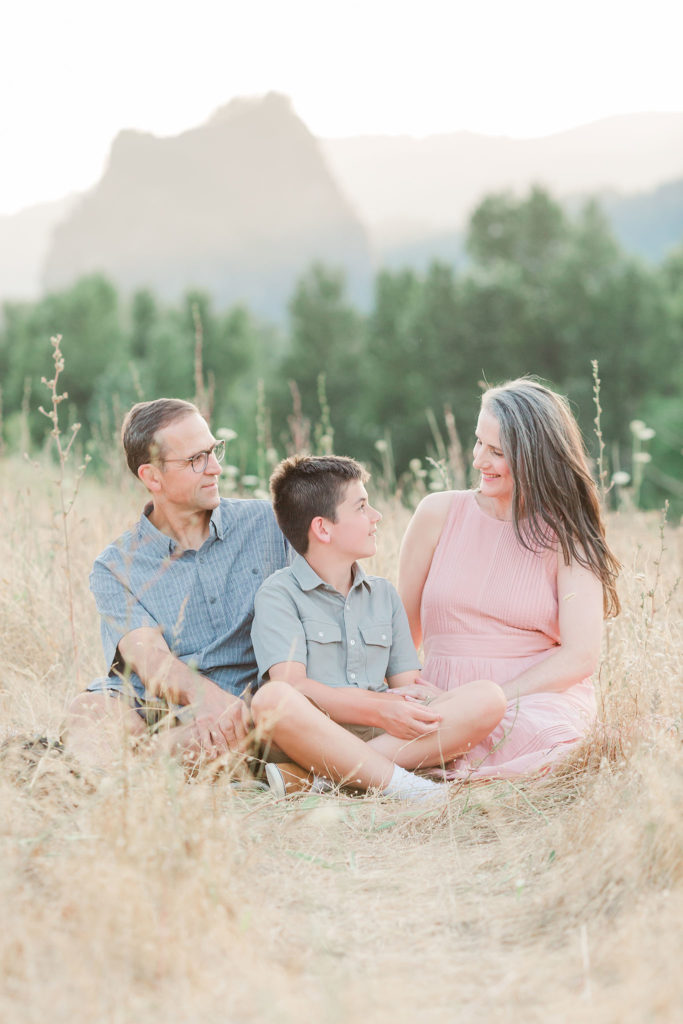family of three seated in a field in front of Beacon Rock for lifestyle family photos near Portland, Oregon