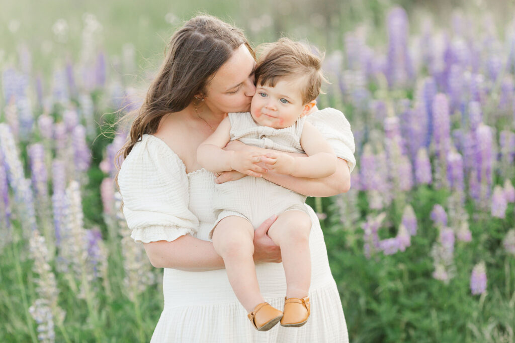 Motherhood photo of mom and baby in a field of purple wildflowers
